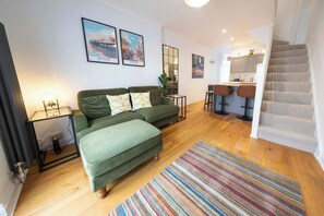 A modern living room with a green sofa, a striped rug, and a kitchen area with bar stools.