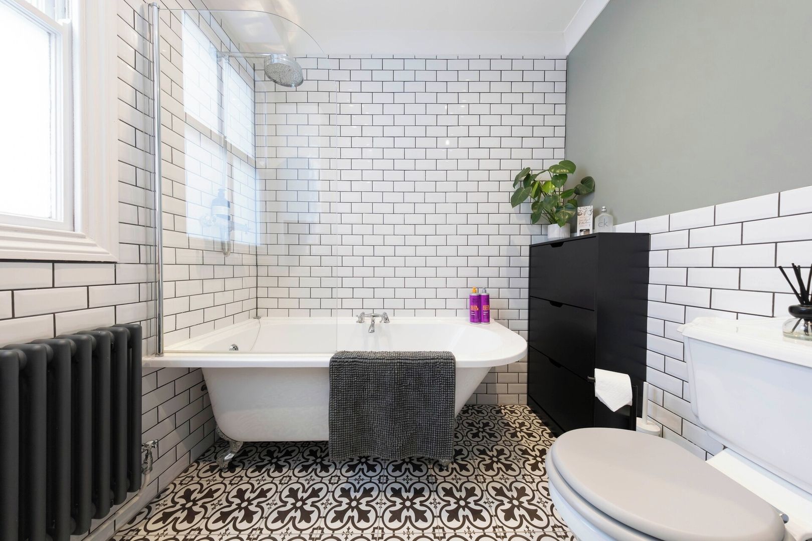 A bathroom with a white bathtub, a toilet, and a radiator.