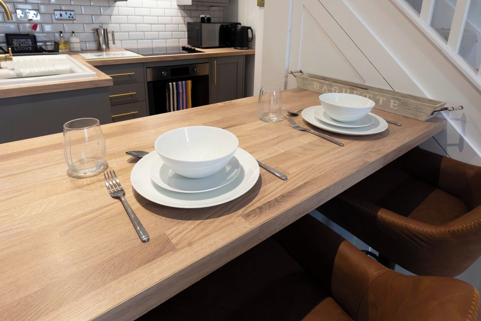 Une cuisine moderne avec un plan de travail en bois, deux bols blancs, un verre et une chaise en cuir marron.