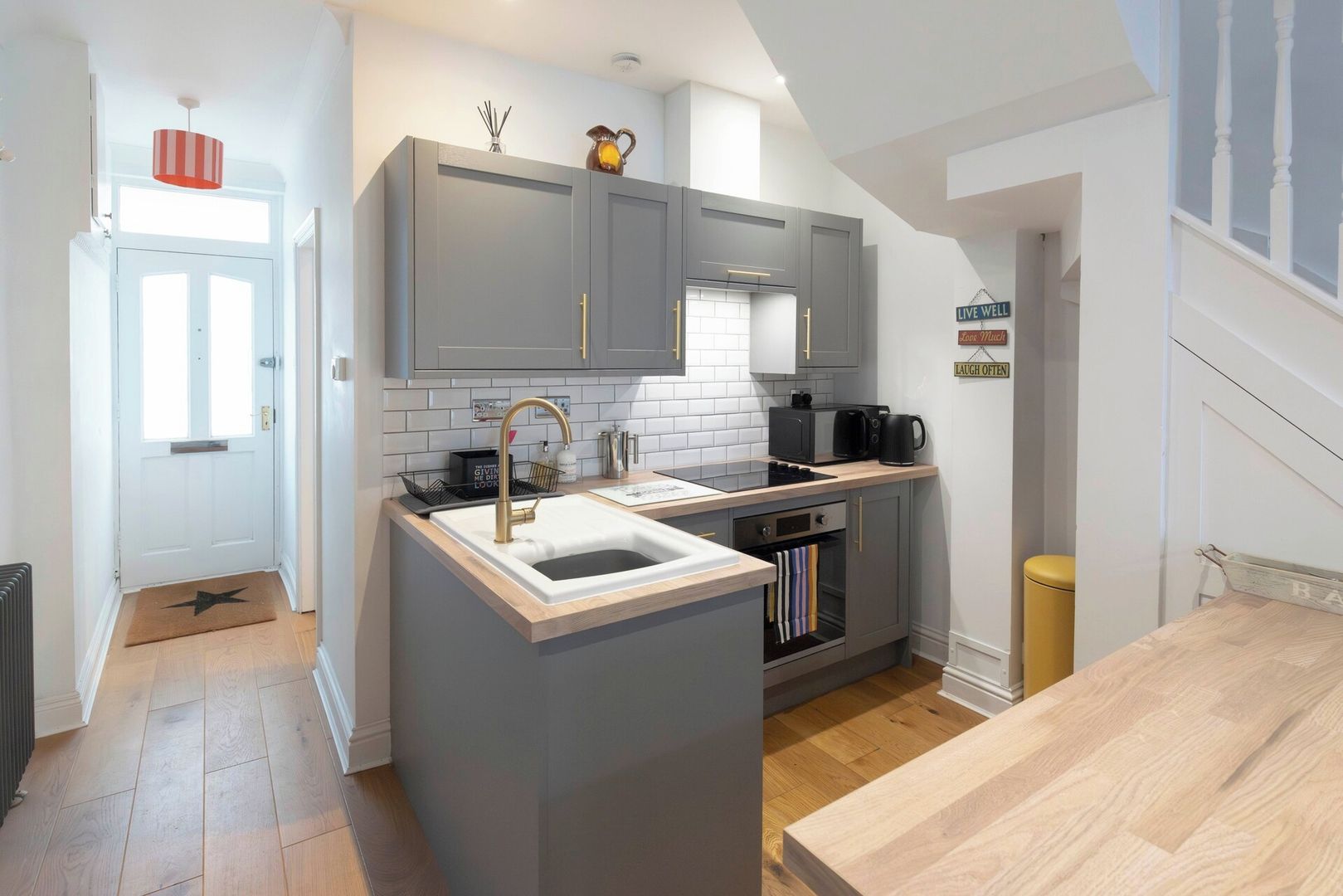 A compact kitchen with grey cabinets, a central island with a sink, a built-in oven, and a coffee machine.