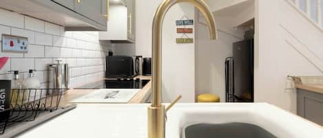 A modern kitchen with a white countertop, a gold faucet, and a black microwave.