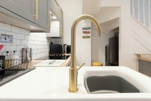 A modern kitchen with a white countertop, a gold faucet, and a black microwave.