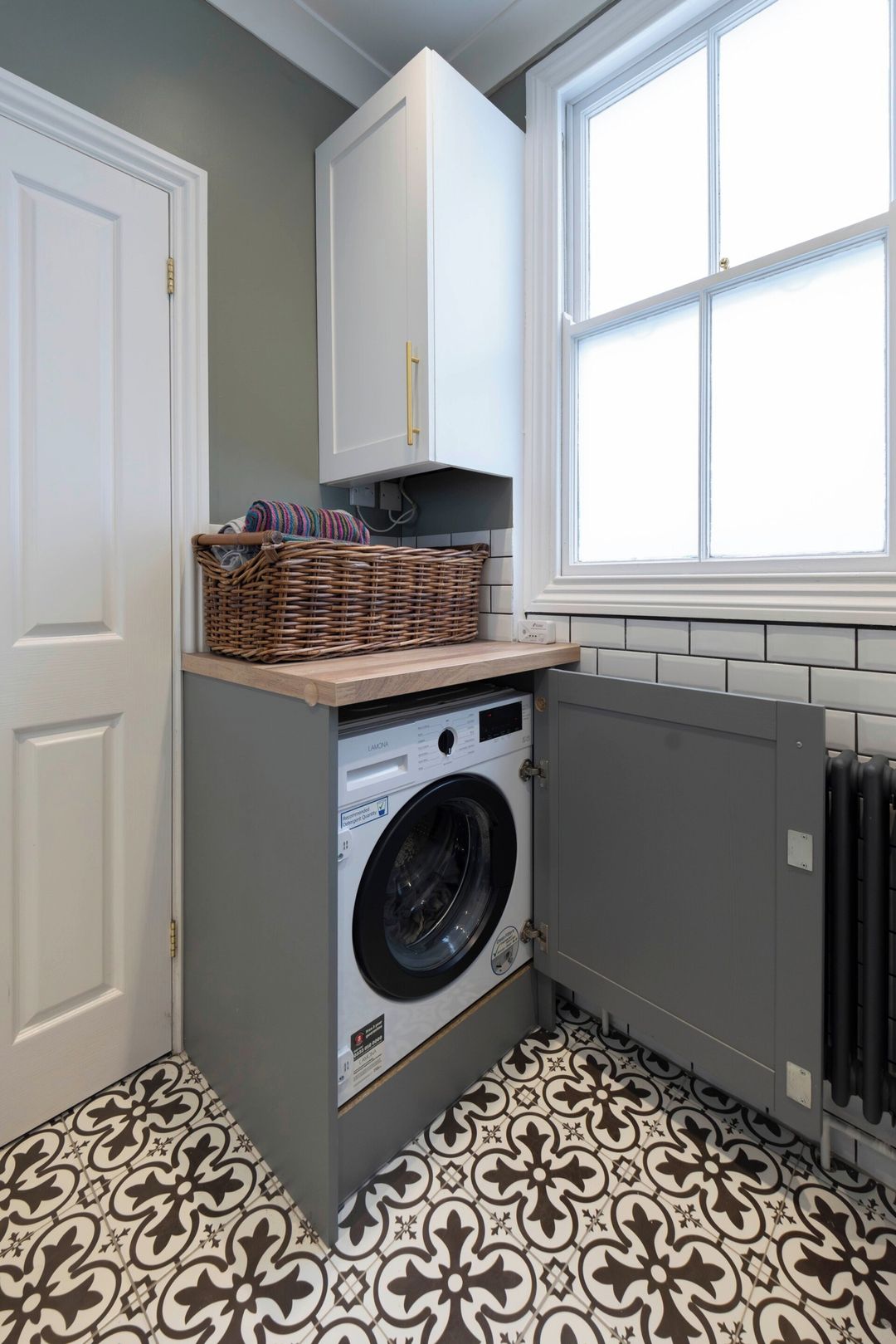 A laundry room with a washing machine, a wicker basket, and a window.