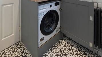 A laundry room with a washing machine, a wicker basket, and a window.