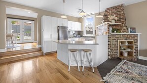 A modern kitchen with white cabinets, a central island with stools, a brick fireplace, and a view to the outside.