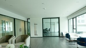 A spacious, modern office with a minimalist design, featuring a mix of seating areas and a glass partition wall. - A charming one-bedroom a condo near the BTS (Bangkok)