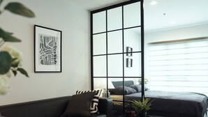 A modern living room with a black sofa, a coffee table, and a large window. - A charming one-bedroom a condo near the BTS (Bangkok)