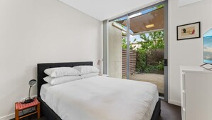 Ein modernes Schlafzimmer mit einem großen Bett, einem Schreibtisch und einer Schiebeglastür, die zu einem Außenbereich führt.