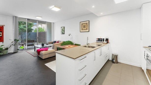 Eine moderne Küche mit einer großen Kochinsel, weißen Schränken und einer Schiebetür zum Balkon.