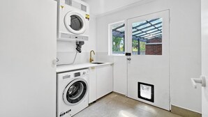 A compact laundry room with a washing machine, dryer, and sink. - Spacious 2-Bed Townhouse with BBQ (Surf Beach)