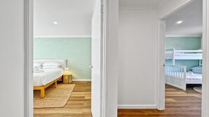 A bedroom with a wooden floor, a bed with white bedding, a nightstand, and a green brick wall. - Spacious 2-Bed Townhouse with BBQ (Surf Beach)