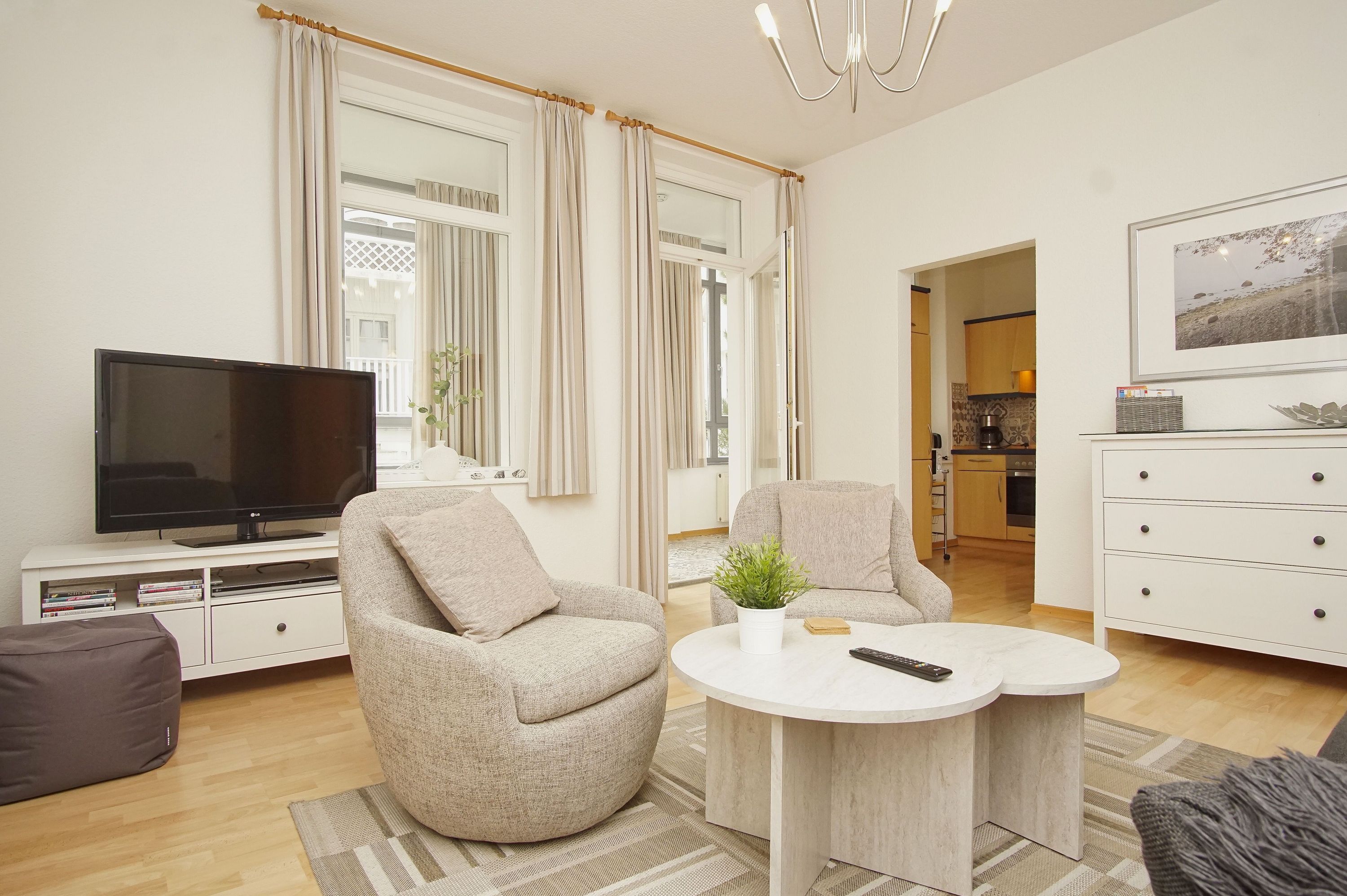 Una sala de estar moderna con un televisor de pantalla plana, dos sillones, una mesa de centro y un comedor con una cocina al fondo.