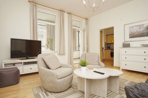 Una sala de estar moderna con un televisor de pantalla plana, dos sillones, una mesa de centro y un comedor con una cocina al fondo.