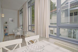 Una habitación con un ventanal grande, una silla blanca, una mesita y una estantería.