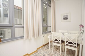 Una habitació amb taula i cadires, un radiador i una finestra amb cortines.
