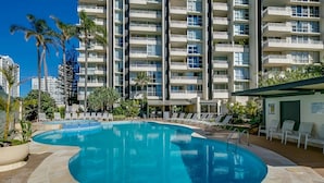 Una piscina con lettini e palme, circondata da un edificio a più piani con balconi.