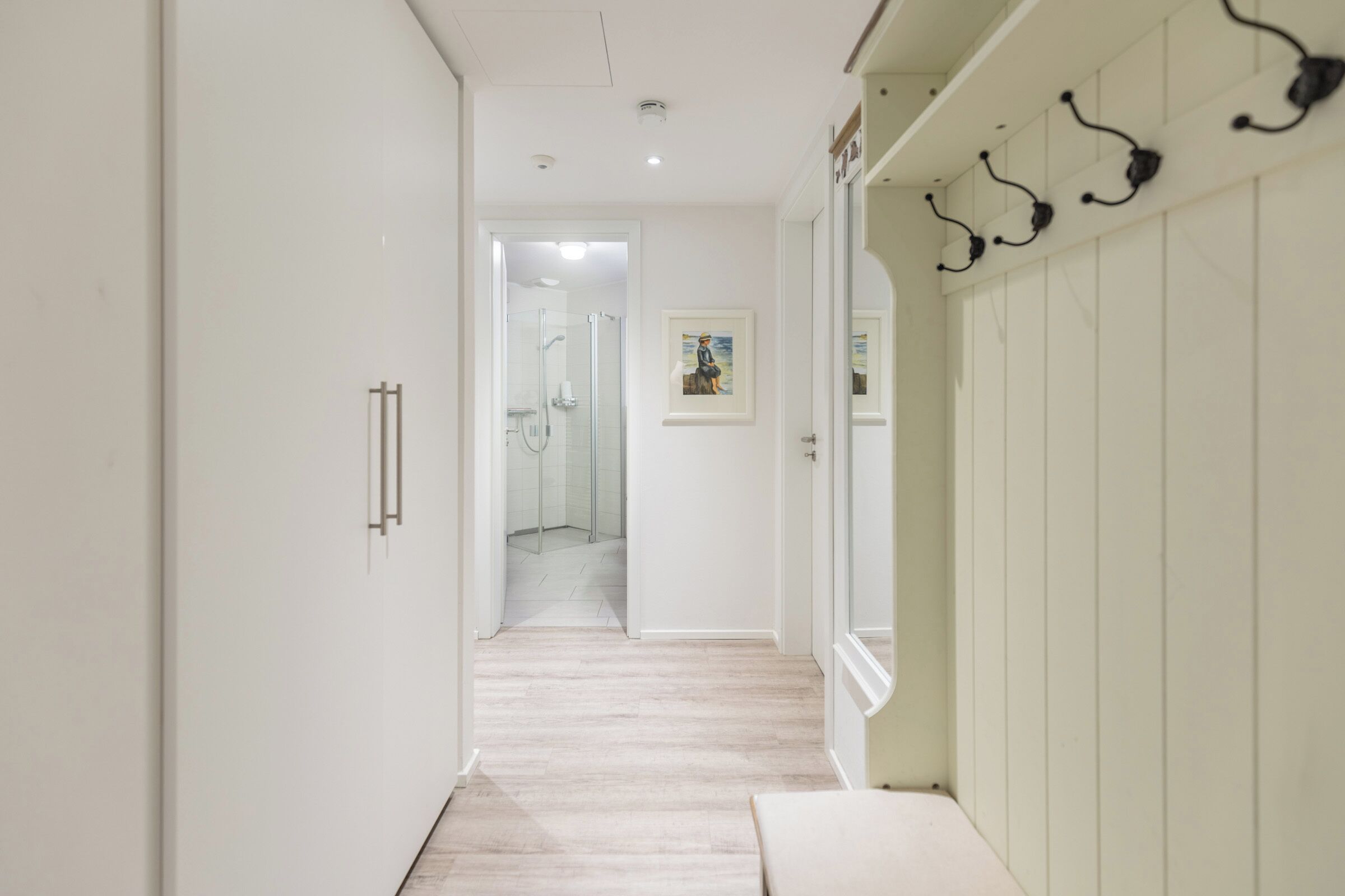 Een gang met een houten vloer, witte muren en een deur naar een badkamer.