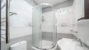 Moderni kylpyhuone, jossa on lasiseinällä varustettu suihku, valkoinen pesuallas ja wc.