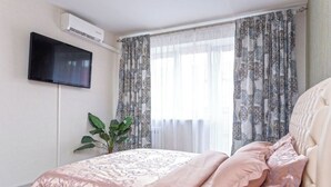 Makuuhuoneessa on sänky, ruukussa oleva kasvi, seinälle asennettu televisio ja kuviollinen verho.
