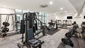 Een moderne sportschool met diverse fitnessapparaten, grote ramen en een flatscreen aan de muur.
