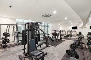 Ein modernes Fitnessstudio mit verschiedenen Trainingsgeräten, großen Fenstern und einem Flachbildfernseher an der Wand.