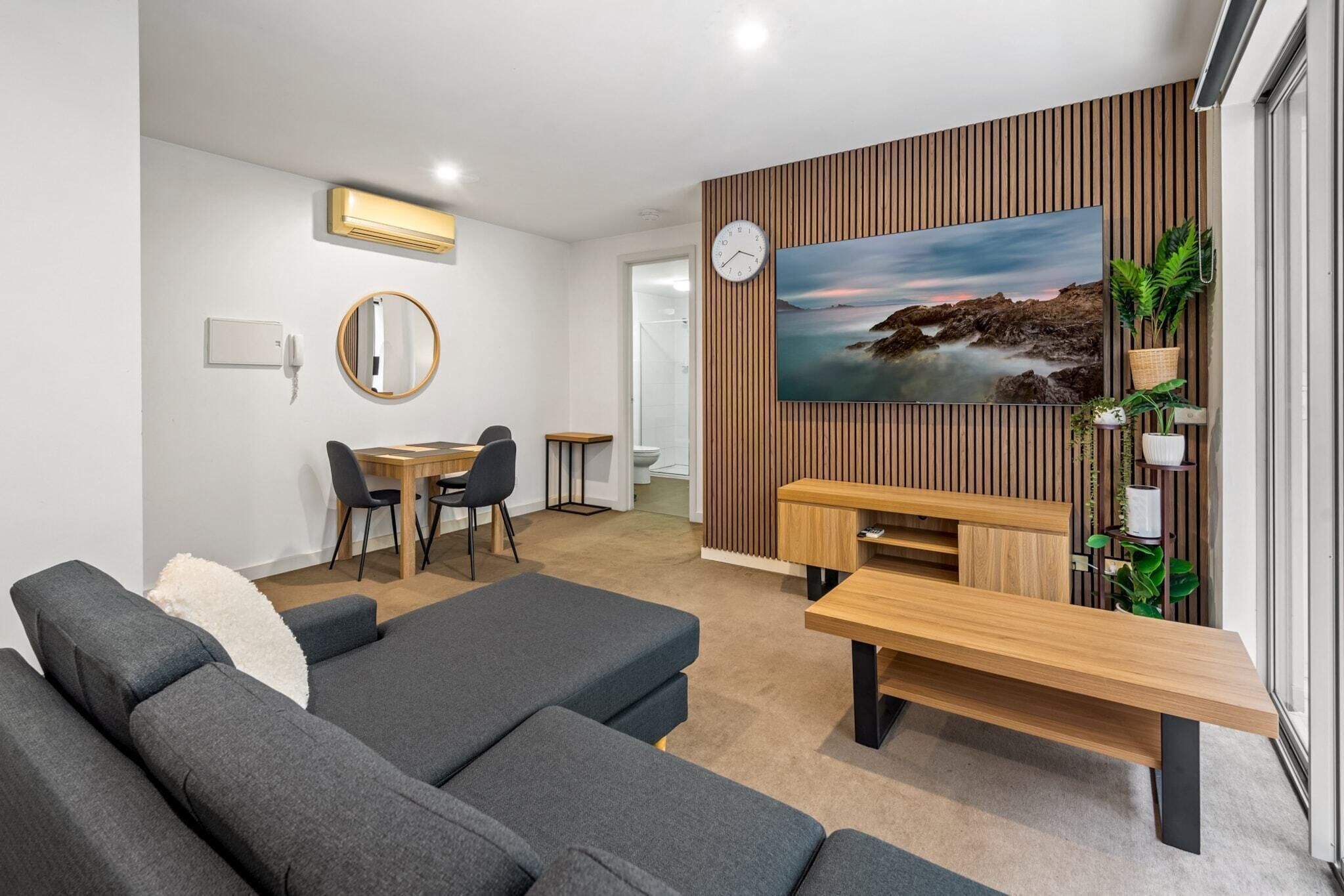 Una sala de estar moderna con un sofá gris, una mesa de centro de madera y un televisor montado en una pared de paneles de madera.