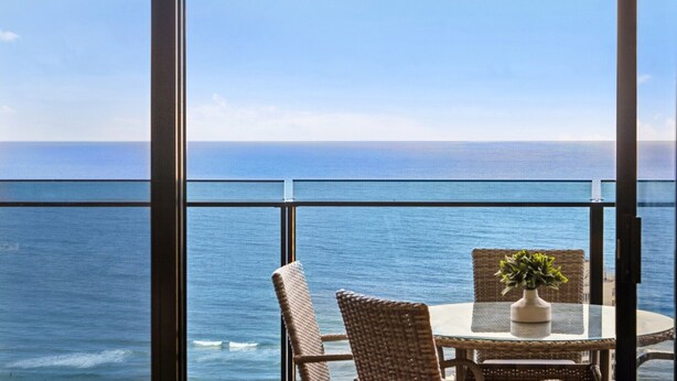 A balcony with a view of the ocean, wicker chairs, and a table with a potted plant. - Circle on Cavill Luxe 2-Bed with Views & Pool (Surfers Paradise)