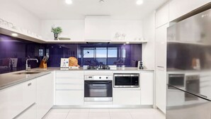 A modern kitchen with white cabinetry, a built-in oven, a microwave, and a stainless steel refrigerator. - Circle on Cavill Luxe 2-Bed with Views & Pool (Surfers Paradise)