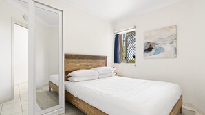 A bedroom with a wooden bed, white bedding, a sliding glass door, and a small window with curtains. - Chic 1-Bed Escape with Parking Bridgeman Downs (Bridgeman Downs)