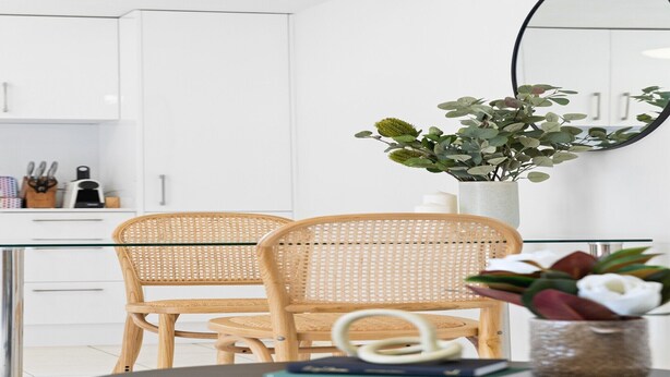 A modern kitchen with white cabinets, a glass table, and a wicker chair. - Chic 1-Bed Escape with Parking Bridgeman Downs (Bridgeman Downs)