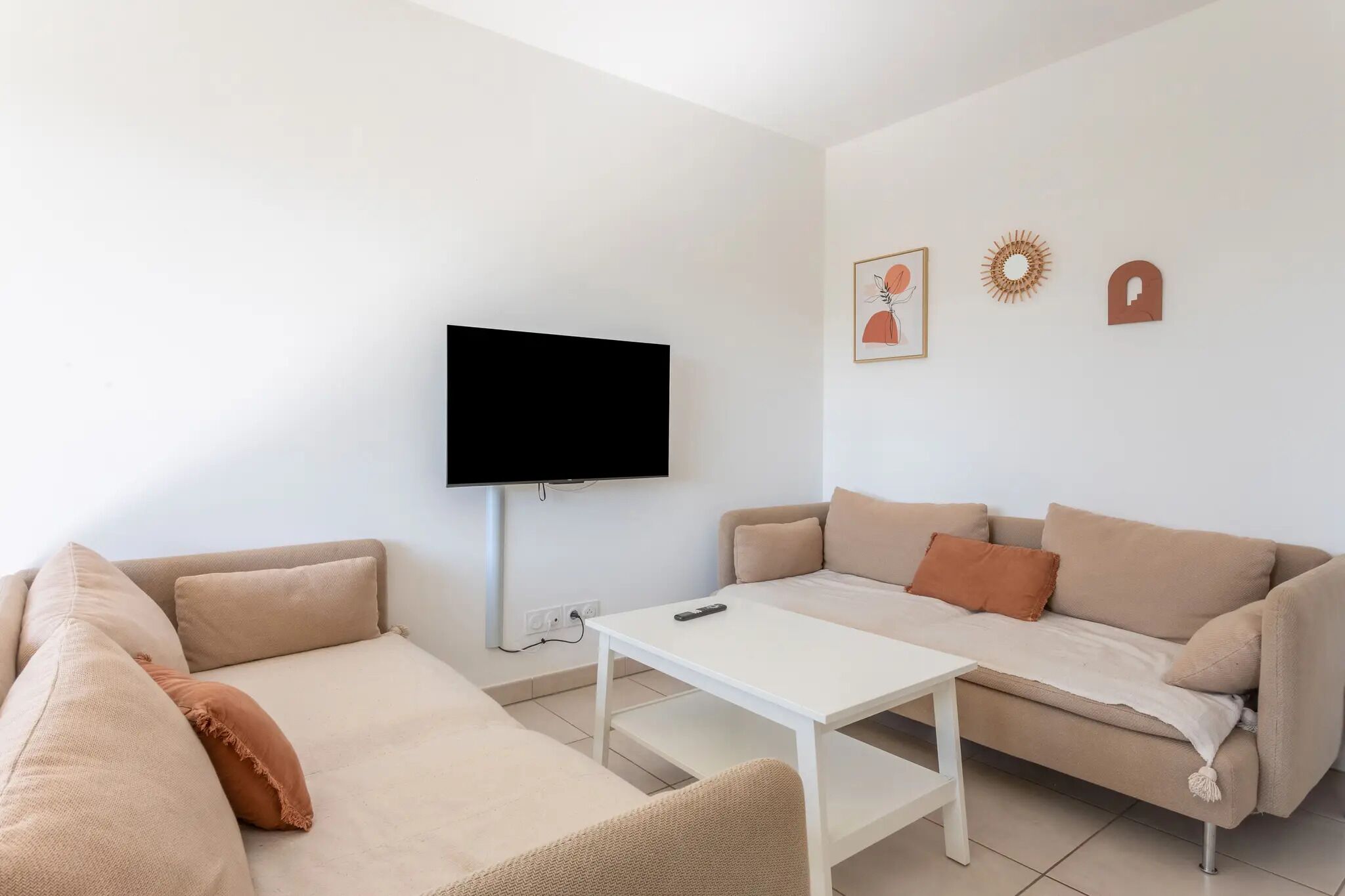 Een moderne woonkamer met een beige bank, een witte salontafel en een flatscreen televisie aan de muur.