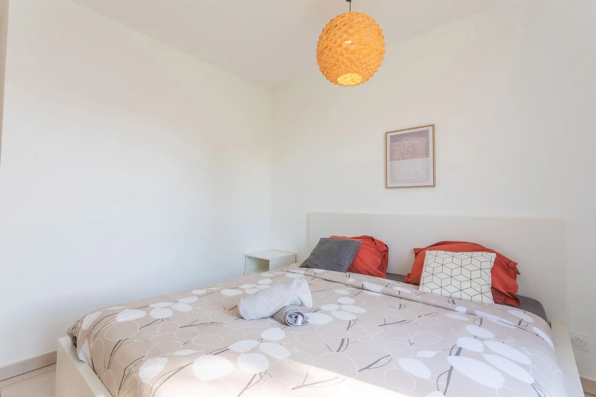 Un lit bien fait, avec une couvre-lit à motifs et des oreillers, une table de chevet et une lampe suspendue.