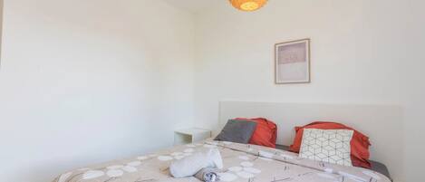 Un lit bien fait, avec une couvre-lit à motifs et des oreillers, une table de chevet et une lampe suspendue.