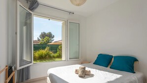 A bedroom with a bed, two pillows, a window with curtains, and a view of greenery outside. - Terrace apartment Puget-sur-Argens (Puget-sur-Argens)