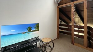 Une pièce avec un téléviseur diffusant une scène de plage, une chaise en osier et une structure de plafond en bois.