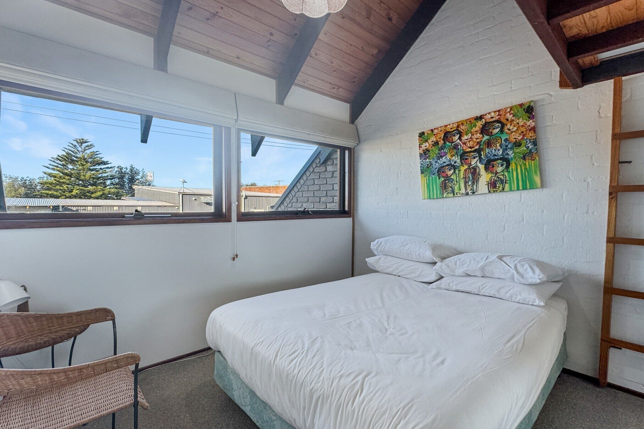 A bedroom with a bed, a chair, a window, and a painting on the wall.