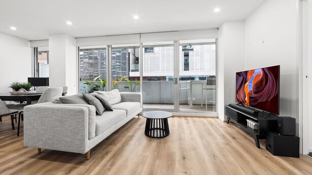 Ein modernes Wohnzimmer mit einem grauen Sofa, einem runden schwarzen Couchtisch und einem Flachbildfernseher auf einem schwarzen Lowboard.