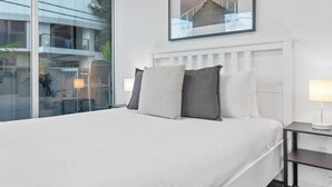 Ein modernes Hotelzimmer mit einem großen Bett, einem Nachttisch mit Lampe und Blick auf den Balkon.