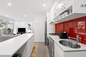 A modern kitchen with white cabinetry, a stainless steel sink, and a red backsplash. - Sleek South Yarra 2-Bed with Alfresco Dining (South Yarra)