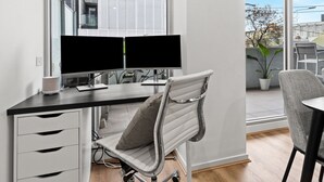 Ein moderner Arbeitsplatz mit Schreibtisch, zwei Monitoren, einem Stuhl und Blick auf die Stadt durch große Fenster.