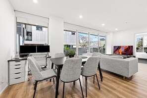 A modern living room with a grey sofa, a dining table with chairs, and a kitchen area with a TV. - Sleek South Yarra 2-Bed with Alfresco Dining (South Yarra)