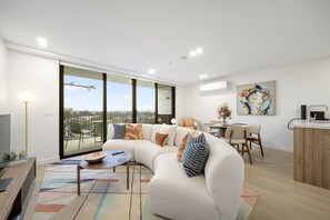 A modern living room with a large sectional sofa, a dining area with a small table and chairs, and a kitchen area with a countertop and sink. - Sleek Inner-City 2-Bed with Swimming Pool & BBQ (Dickson)