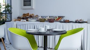Montaje de un bufé de desayuno con diversos alimentos, como panes, frutas y postres, dispuestos sobre una mesa con mantel blanco.