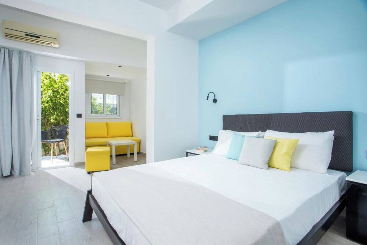 Una habitación de hotel moderna con una cama grande, un sofá amarillo y una mesita pequeña.