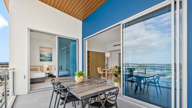 Un balcón moderno con una mesa de comedor, sillas y plantas en macetas.