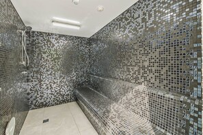 A modern bathroom with mosaic tile walls, a bench, and a shower area. - Waterfront 2-Bed Oasis - Pool, Steam, Jacuzzi, Gym (Bokarina)