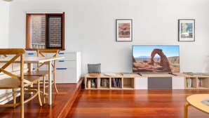 Uma sala de estar moderna com uma mesa de jantar de madeira, cadeiras, uma televisão de tela plana e uma estante de livros.