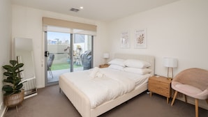 Une chambre moderne avec un grand lit, une table de chevet, une chaise et une porte-fenêtre coulissante donnant sur un espace extérieur.