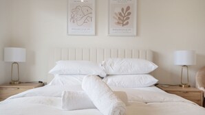 Un lit bien fait, avec du linge de lit blanc et une serviette enroulée, deux lampes de chevet et deux œuvres d’art encadrées accrochées au mur.
