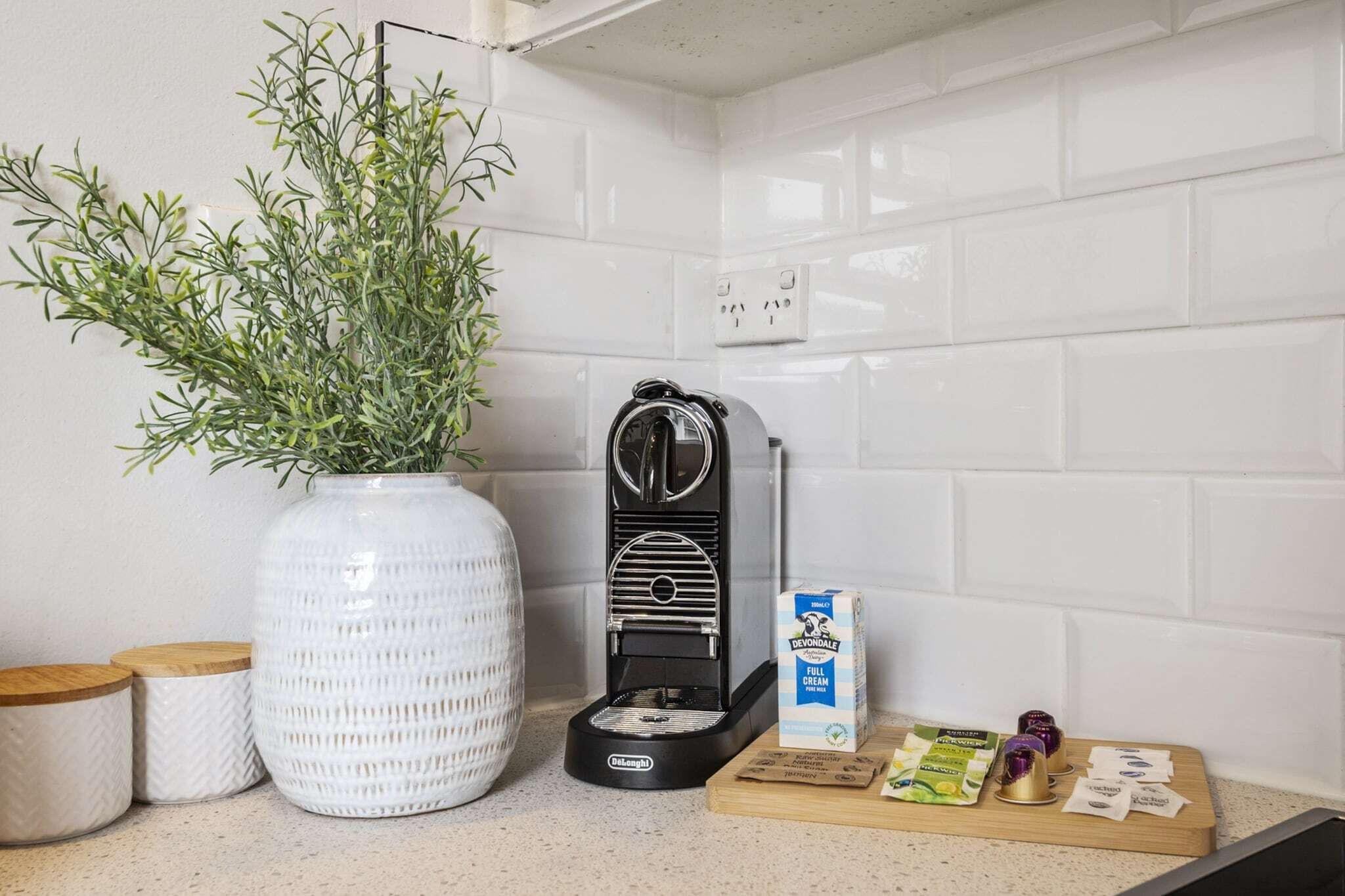 A kitchen counter with a coffee machine, a potted plant, a box of Devondale full cream milk, and some coffee pods.